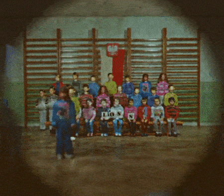 a group of school children posing for a class photo in a gym with some kids silhouettes appearing in front randomly